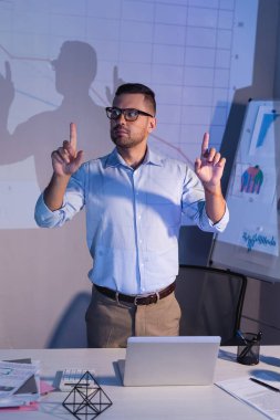 Ofisteki dijital grafiklerin yanındaki parmaklarıyla gözlüklü iş adamı