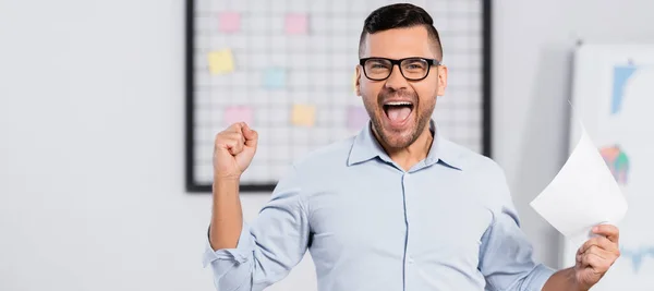 amazed businessman in glasses holding document in office, banner