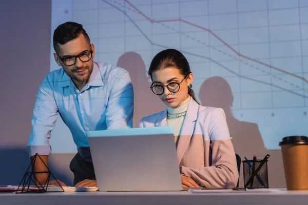 Uomini Affari Occhiali Guardando Computer Portatile Con Grafici Digitali Parete — Foto Stock