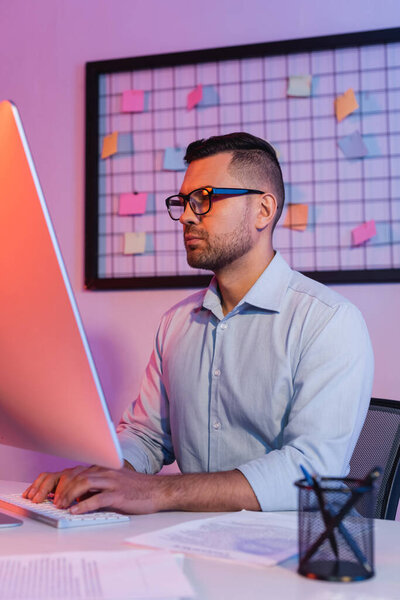 бизнесмен в очках печатает на клавиатуре компьютера и смотрит на монитор 