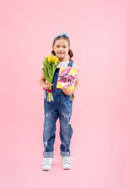 Uzun boylu mutlu bir çocuk lale ve tebrik kartı tutuyor. Seni seviyorum anne, pembe harflerle. 