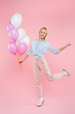 Uzun boylu, neşeli bir kadın. Zıplıyor ve pembe üzerinde balonlar tutuyor.