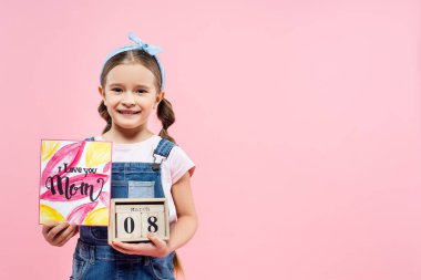 Mutlu çocuk elinde tebrik kartı tutuyor. Seni seviyorum anne. Pembe üzerine 8 yürüyüş izole edilmiş tahta küplerle mektup yazıyor. 