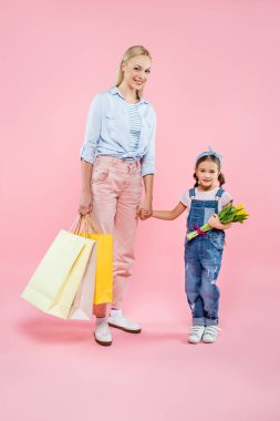 Alışveriş torbalarıyla mutlu bir anne ve pembe laleli bir kız. 