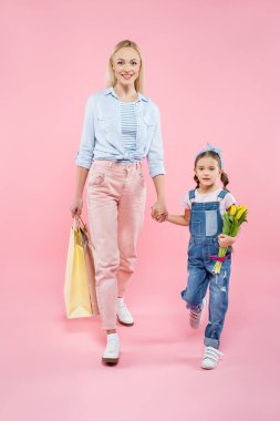 Tam boy anne, alışveriş torbaları ve pembe üzerinde yürüyen laleli kız. 