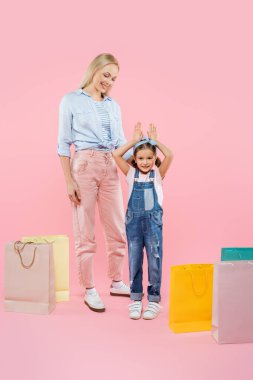 Mutlu bir anne, pembe poşetlerin yanında tavşan kulaklı bir çocuğa bakıyor.