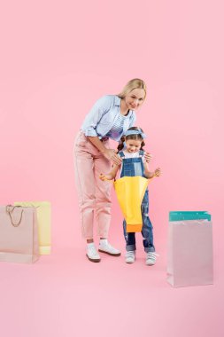 Mutlu bir anne ve gülümseyen bir kız çocuğu pembe bir alışveriş çantasına bakıyor.