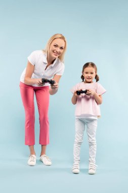 KYIV, UKRAINE - 25 Kasım 2020: Mavi üzerinde joystickler tutan mutlu anne ve kız tam boy