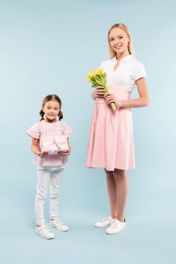 Hamile bir annenin yanında mavi lalelerle bekleyen bir çocuk.