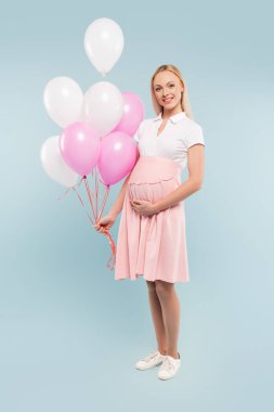 Mavi üzerinde balon tutan hamile bir kadın.
