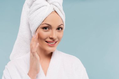 Bornozlu mutlu kadın mavi üzerine kozmetik krem sürüyor.