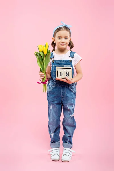 全长快乐的孩子拿着郁金香和木制立方体 上面有8个带着粉红字的行军字母 — 图库照片