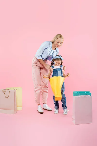 全长快乐的母亲和笑容满面的女儿看着粉色购物袋 — 图库照片