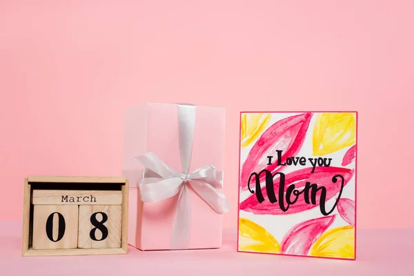 wooden calendar with 8 march lettering near gift box and greeting card on pink