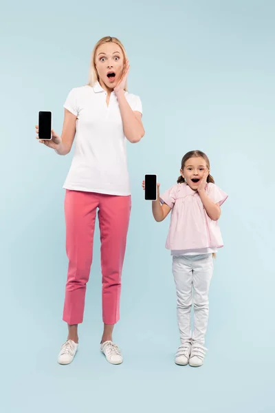 Full Length Shocked Mother Daughter Holding Smartphones Blank Screen Blue — Stock Photo, Image