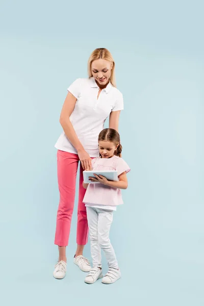 全长快乐的母亲和女儿看着蓝色的数码平板电脑 — 图库照片