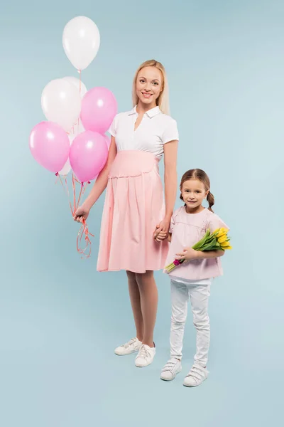 全身上下都是快乐的孕妇 她在女儿身边拿着气球 蓝色上有郁金香 — 图库照片