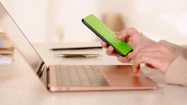 Bilgisayarda dokunmatik ped kullanan ve elinde akıllı telefon tutan bir kadın görüntüsü.