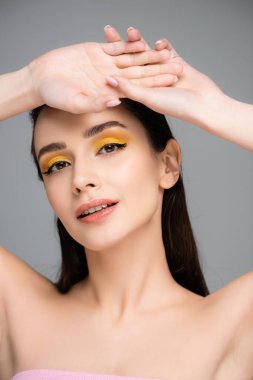 Sarı göz farı olan esmer genç bir kadın gri kameraya bakıyor.