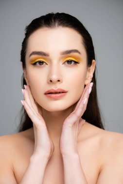 Sarı göz farı olan esmer kadın gri kameraya bakıyor.