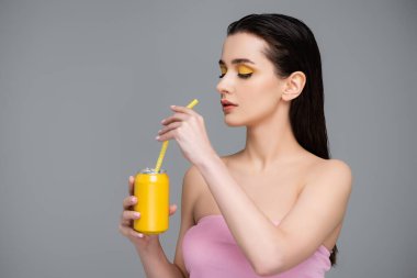 Sarıyı elinde meşrubatla tutan esmer genç bir kadın ve gri üzerinde izole edilmiş samanlara bakıyor. 