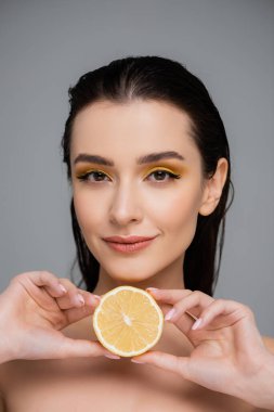 Çıplak omuzlu, olgun limonun yarısını tutan genç bir kadın. 