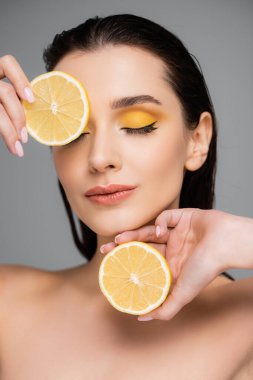 Çıplak omuzlu, olgun limon parçalarını tutan genç bir kadın. Gri renkte izole edilmiş. 