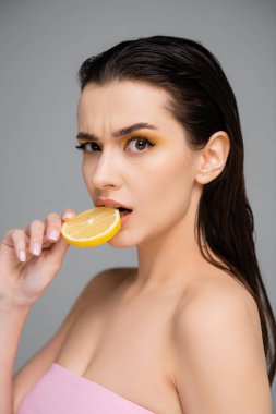 Şaşırmış, çıplak omuzlu, dilimlenmiş limon yiyen genç bir kadın. 