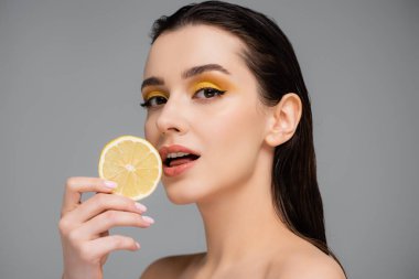Gri renkte dilimlenmiş limon tutan çıplak omuzlu esmer bir kadın. 