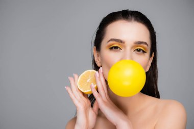 Genç esmer, makyajlı, sarı sakızlı ve limonun yarısını gri renkte tutan kadın.