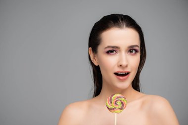 Gri üzerinde lolipop tutan pembe gözlü genç kadın şaşırdı. 
