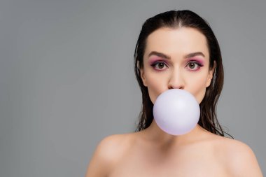 brunette woman with bare shoulders blowing bubblegum isolated on grey clipart