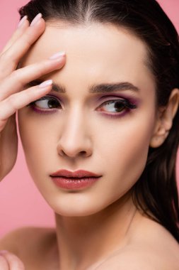 Çıplak omuzlu ve makyajlı genç bir kadın pembe üzerine izole edilmiş bir şekilde bakıyor. 