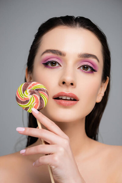 young woman with pink eye shadows holding lollipop isolated on grey 