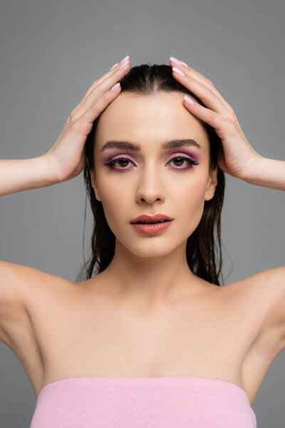 woman with pink eye shadows adjusting hair isolated on grey 