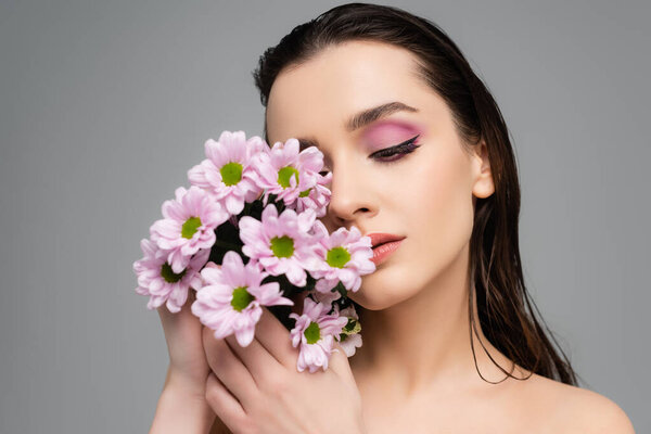 брюнетка молодая женщина с розовыми тенями глаз держа цветы изолированы на сером 