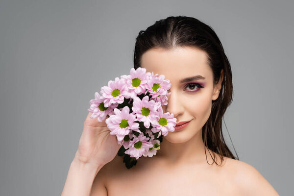 молодая женщина с розовыми тенями для глаз покрывает лицо цветами, изолированными на сером 