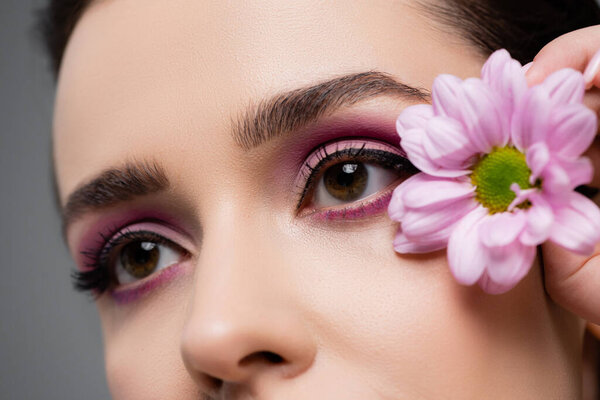 close up of sensual woman with pink eye shadows holding flower isolated on grey