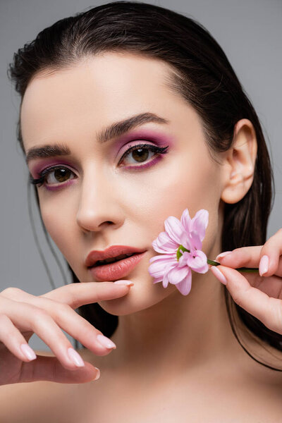 молодая чувственная женщина с розовыми тенями для глаз держа цветок изолирован на сером