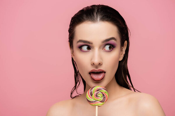 молодая женщина с тенями для глаз торчащих язык рядом с леденец изолирован на розовый 