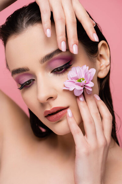 sensual young woman with eye shadows holding flower isolated on pink