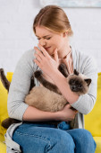 Žena s alergií škrábání nos a držení kočka 