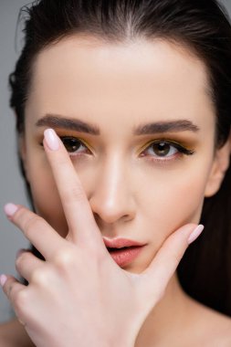 Makyajlı genç esmer kadının yakın çekim görüntüsü. Gri renkli kameraya bakıyor.
