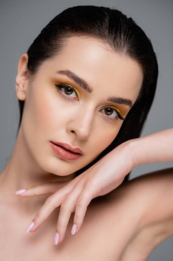 young woman with yellow eyeshadow looking at camera isolated on grey clipart