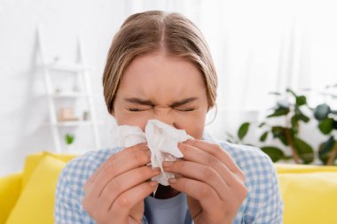 Woman holding napkin near nose during allergy at home  clipart