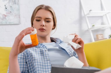 Woman with allergy holding napkin and jar with pills on blurred foreground  clipart
