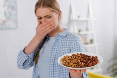 Plate with nuts in hand of woman with allergy on blurred background  clipart