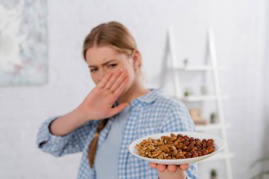 Plate with nuts in hand of woman with allergy showing stop gesture on blurred background  clipart