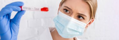 Doctor in medical mask holding test tube with blood sample during allergy test on blurred foreground, banner 