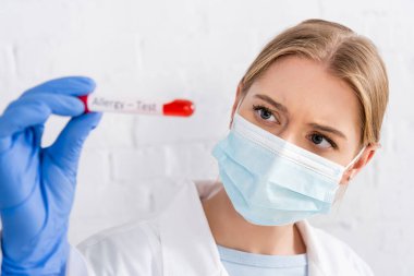 Tıbbi maskeli doktor ön planda alerji testi sırasında tüpü tutuyor. 
